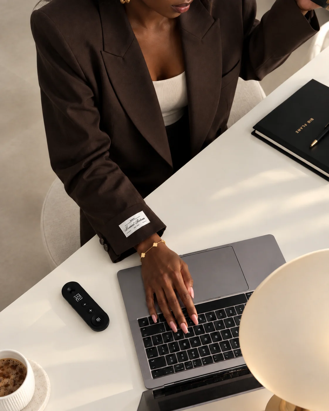 Femme entrepreneure en blazer marron travaillant sur son ordinateur portable, carnet de notes à côté